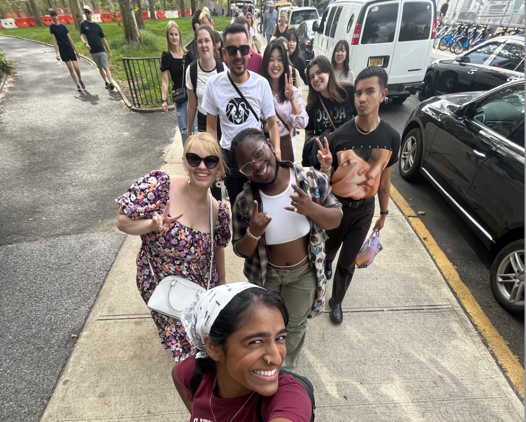 Group of student and their advisor from different cultures and countries smile together in a selfie in the streets of Brooklyn, NY