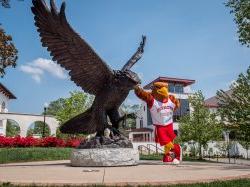 a photo of Rocky the mascot next to the Red Hawk Statue