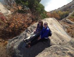 在一个阳光明媚的日子里，两个女孩坐在一块岩石上俯瞰风景