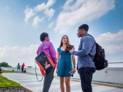 三个学生站在校园里的一栋建筑外聊天.