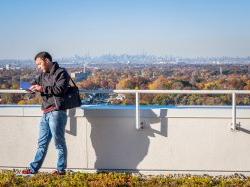 A student standing behind the CELS building reading a book with New York City in the distance.