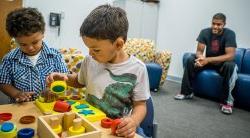Image of children in a clinicial setting playing with blocks while parent looks on.