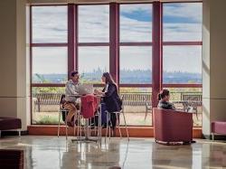 students sitting at a high-top table in open atrium. wall of windows with NYC skyline is in the background