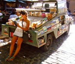 阿根廷，一名学生倚在装满书的小货车上看书.