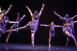Photo of six dancers leaping toward a central point.