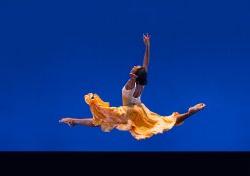 舞者在空中跳跃的照片，裙子与蓝色背景形成对比
