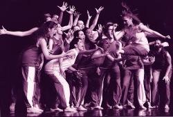Photo of large troupe of dancers crowded close on stage.